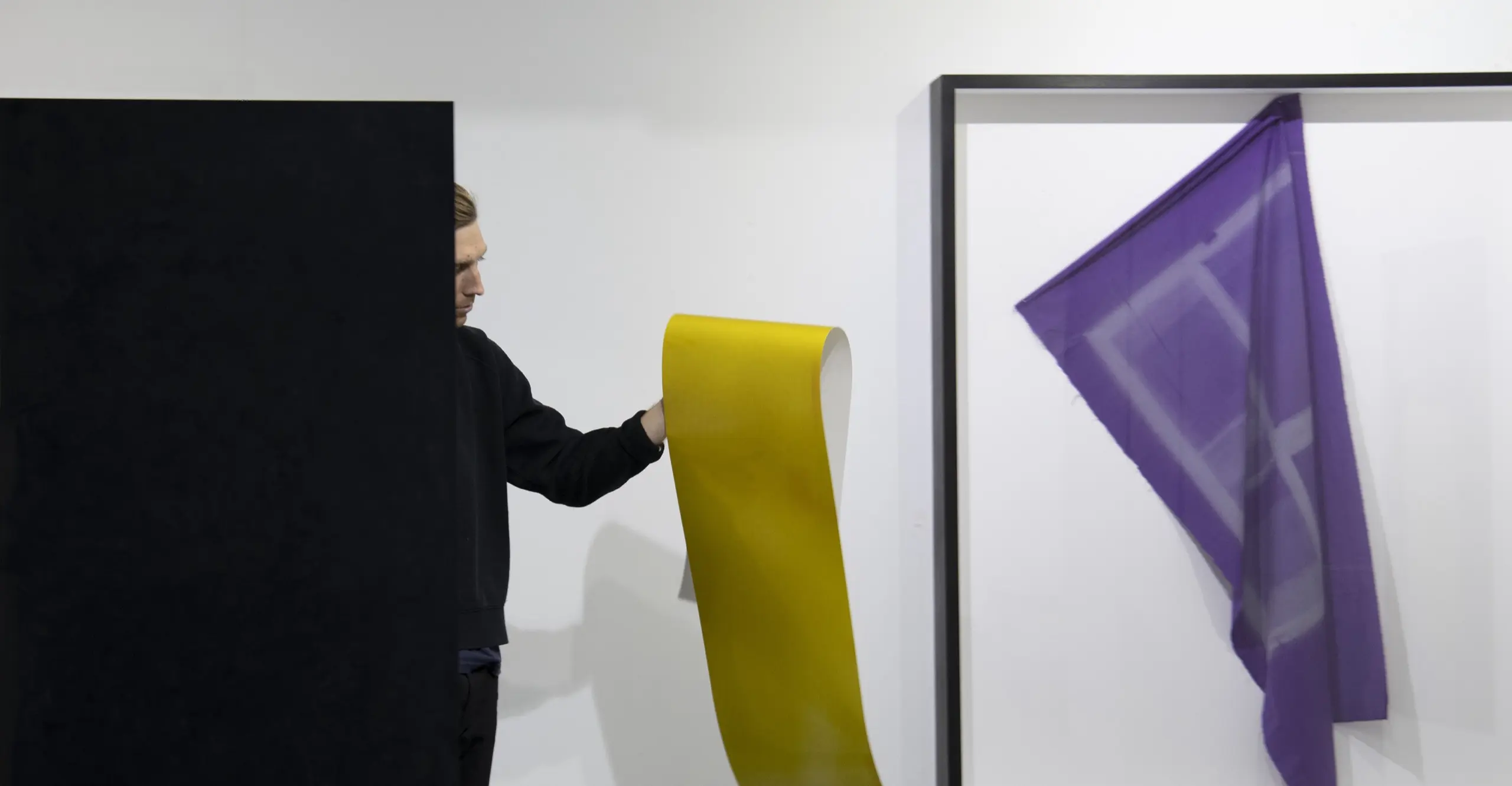 Photograph featuring Tom Lovelace partially obscured while holding a gold paper with a framed abstract purple work